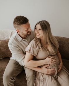 a man and woman sitting on a couch cuddling each other with their arms around one another