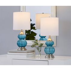 two blue glass table lamps sitting on top of a white dresser next to a mirror