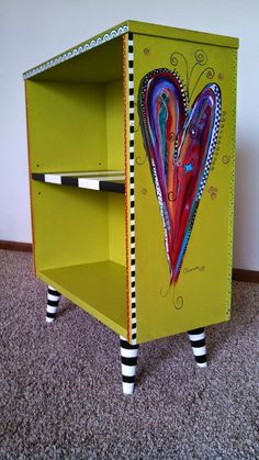 a yellow cabinet with two drawers on the bottom and one drawer painted like a heart