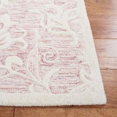 a white rug with pink and red designs on the floor in front of a wooden floor