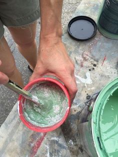 a man is painting the outside of a bucket with green and white paint on it