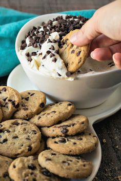 a person scooping ice cream out of a bowl with chocolate chip cookies on the side