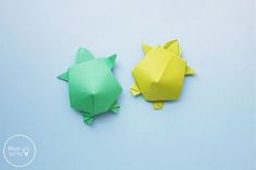 two origami animals sitting next to each other on a blue surface, one is green and the other is yellow