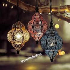 three colorful lanterns hanging from a tree branch with lights in the background and blurry boke patterns on them