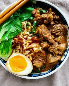 a bowl filled with noodles, meat and an egg next to chopsticks on a table