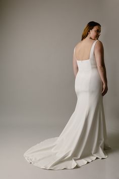 a woman in a white wedding dress is looking back at the camera while standing against a gray background