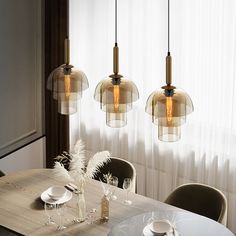 a dining room table with plates and glasses on it, next to three hanging lights