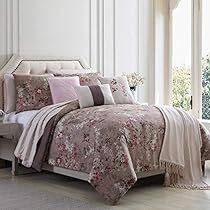 a bed with pink and grey comforters in a white room next to a window