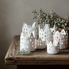 white candles are sitting on a table with greenery in front of them and some houses