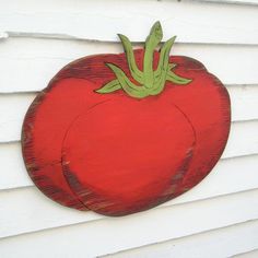 a red painted tomato hanging on the side of a white building with green stems sticking out of it