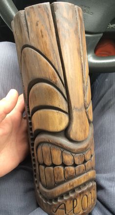 a person holding a wooden carved mug in their hand and wearing a blue shirt behind the steering wheel