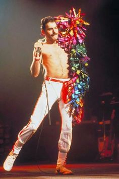 a shirtless man in white pants holding a pole with colorful streamers on it