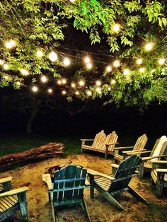 there are many chairs and lights hanging from the trees in the yard at night time