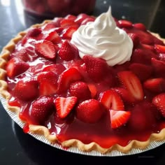 a pie with strawberries and whipped cream on top is sitting on a black table