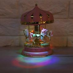 a pink and gold carousel with horses on it's sides is lit up by rainbow light