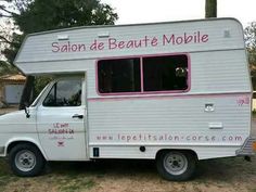 a white truck with pink writing on the side parked in front of some trees and grass