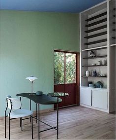 a dining room with green walls and white shelves on the wall, along with two chairs