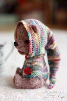 a small teddy bear wearing a knitted sweater sitting on top of a white table