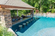 an outdoor swimming pool surrounded by stone pillars and a covered gazebo with seating area next to it