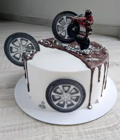 a white cake with a car and wheels on it's side, covered in chocolate icing