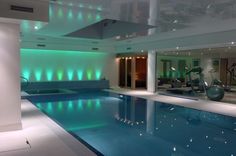 an indoor swimming pool with exercise equipment in the background and green lights on the ceiling