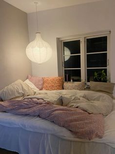 an unmade bed with pillows and blankets on it in front of two large windows