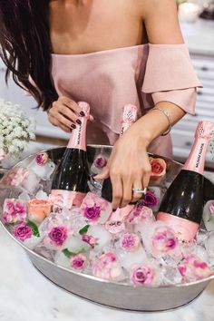 a woman pouring champagne into an ice bucket filled with pink flowers and roses in it