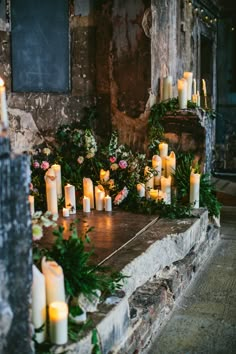 many lit candles are placed on a stone ledge in front of flowers and greenery