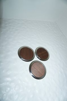 three wooden buttons sitting on top of a white bed sheet with water droplets around them