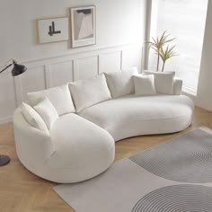 a large white couch sitting on top of a wooden floor next to a lamp and rug