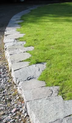 a stone path in the middle of a grassy area next to a parked car on a street