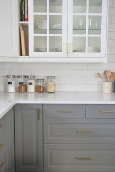 a kitchen with gray cabinets and white subway backsplash, gold pulls on the cabinet doors