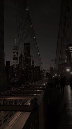 people walking across a bridge at night with the city lights in the backround