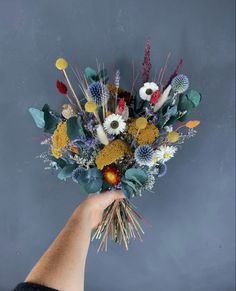 a hand holding a bouquet of flowers against a gray background with grass and wildflowers