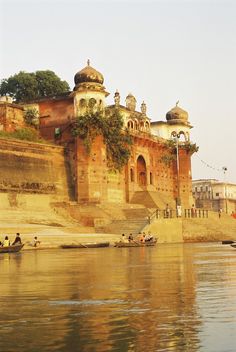 some people are sitting on the bank of a body of water near an old building