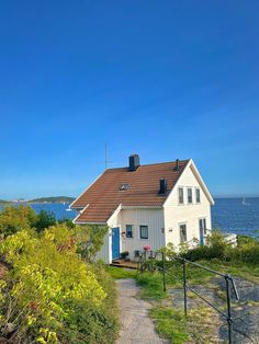 a white house sitting on top of a lush green hillside next to the ocean with a blue door