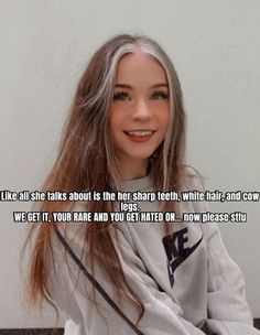 a woman with long hair sitting on the floor next to a white wall and smiling at the camera