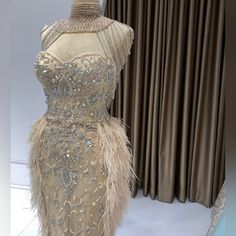 a mannequin with feathers and beading on display in front of curtained windows