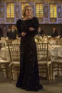 a woman in a long black dress standing next to a table with chairs and tables