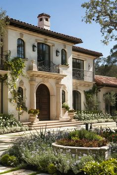 a large white house with lots of plants and flowers around it's front entrance