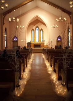 an empty church filled with lots of pews and decorated with branches, lights and candles