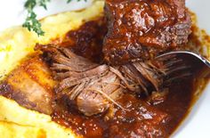 a close up of meat and gravy on top of mashed potatoes with a fork