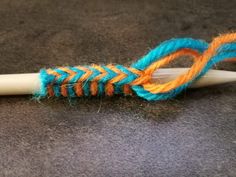 a crochet hook with an orange and blue yarn on it next to a white knitting needle