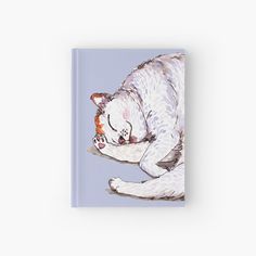 a white cat sleeping on top of a blue book hardcover journal with an illustration of a dog's face