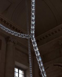 a cross made out of crystal beads hanging from the ceiling in a building with two windows