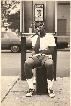 a man sitting on top of a box talking on a cell phone next to a parking meter