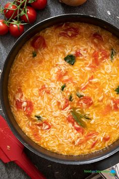 a pot filled with rice and tomatoes on top of a table next to utensils