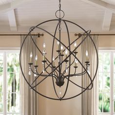 a chandelier hanging from the ceiling in a living room with windows and curtains