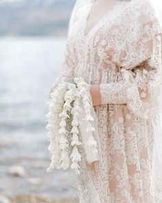 a woman in a white dress holding a bouquet of flowers near the water's edge