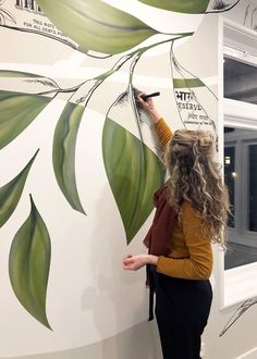 a woman writing on a wall with green leaves